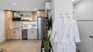 Eine moderne Küche mit integrierten Geräten, einem Geschirrspüler und einem Kühlschrank. Auf dem Boden steht eine Pflanze und an der Wand hängt ein weißer Bademantel.