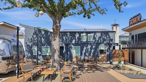 Ein modernes Hotel mit einem großen Baum im Innenhof, Sitzgelegenheiten im Freien und blauem Himmel.