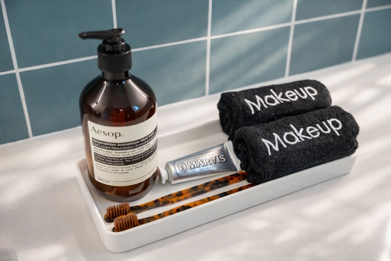 Ein Badezimmer-Waschtisch mit Pflegeprodukten, darunter eine Flasche Aesop Handseife, eine Tube Marvis Handseife und zwei schwarze Handtücher mit der Aufschrift 'Makeup'.