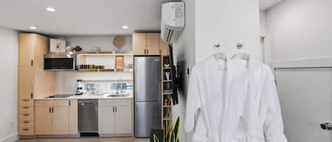 A modern kitchen with built-in appliances, a dishwasher, and a refrigerator. There is a plant on the floor and a white robe hanging on the wall.