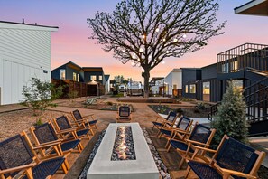 Une cour avec des fauteuils de jardin, un foyer et un grand arbre.