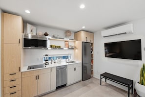 A modern kitchen with stainless steel appliances, a built-in microwave, and a flat-screen TV mounted on the wall. - Stylish King casita, minutes to TCU & Stockyards (Fort Worth)