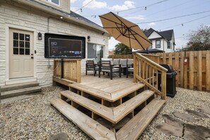 Eine Holzterrasse mit Sitzgelegenheiten im Freien und einem an der Wand befestigten Fernseher.