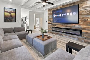 Ein modernes Wohnzimmer mit einem an einer Holzwand befestigten Flachbildfernseher, grauen Sofas und einem kleinen Tisch mit einer Pflanze.