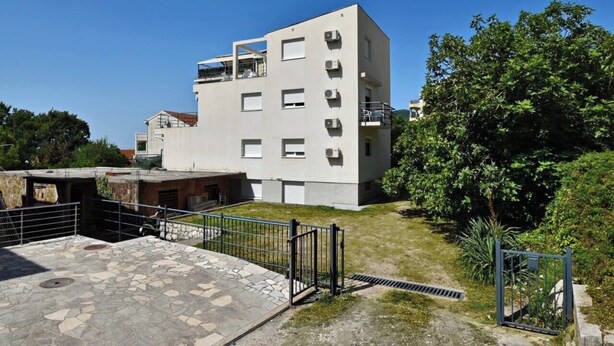 A multi-story building with a flat facade, a gated entrance, and a small courtyard with a stone pathway. - Quiet Garden Studio w/ Private Entrance & Parking (Budva)