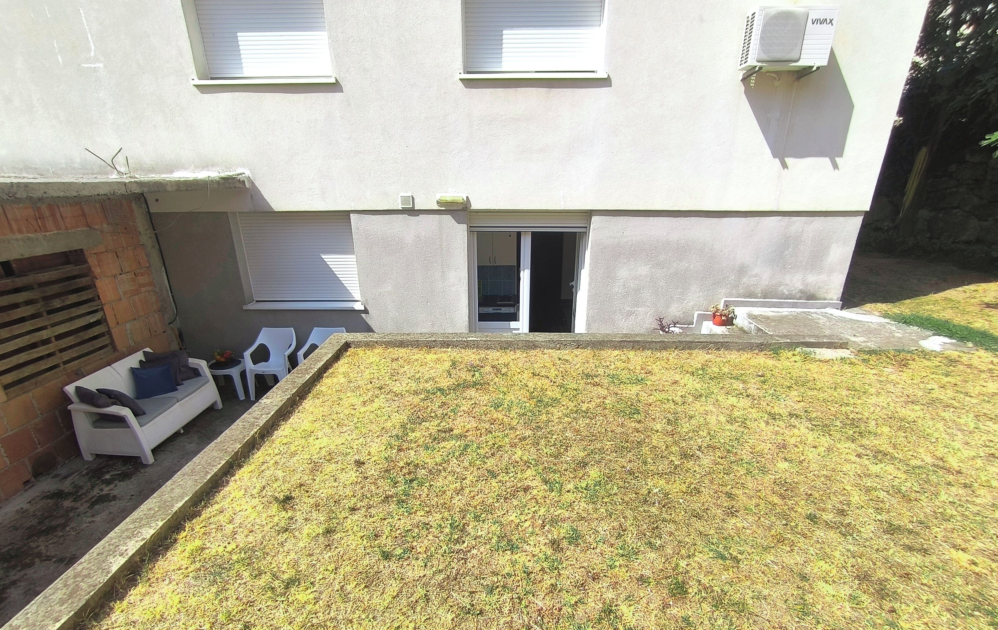 A building with a flat facade, a visible entrance, and a small garden area with grass and a planter.