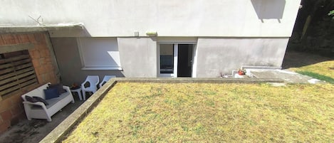 A building with a flat facade, a visible entrance, and a small garden area with grass and a planter.