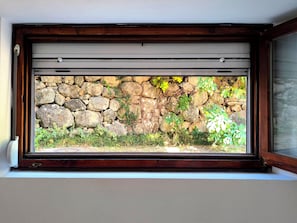 Ein Fenster mit einer Steinmauer und Pflanzen im Hintergrund.