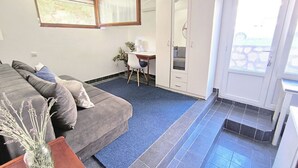 A room with a sofa, a small table with a vase, a desk with a chair, and a balcony with a door. - Quiet Garden Studio w/ Private Entrance & Parking (Budva)