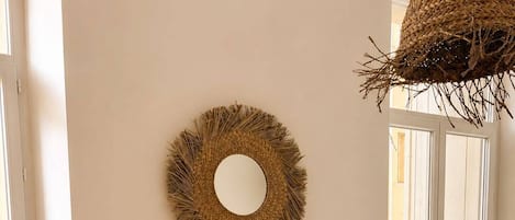 A room with a round mirror on the wall, a round table with chairs, and a woven basket hanging from the ceiling.