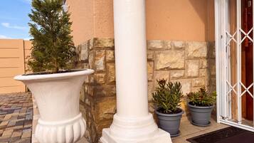 A building corner with a white column, a potted plant, and a stone wall.