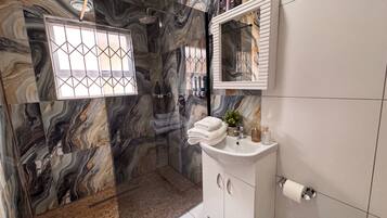 A bathroom with a marble wall, a glass shower enclosure, a sink with toiletries, and a mirror.