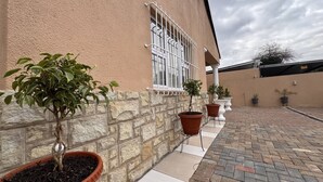 A building with a stone wall, a window with metal bars, and potted plants along the wall. - Saob Property-south AF (Germiston)