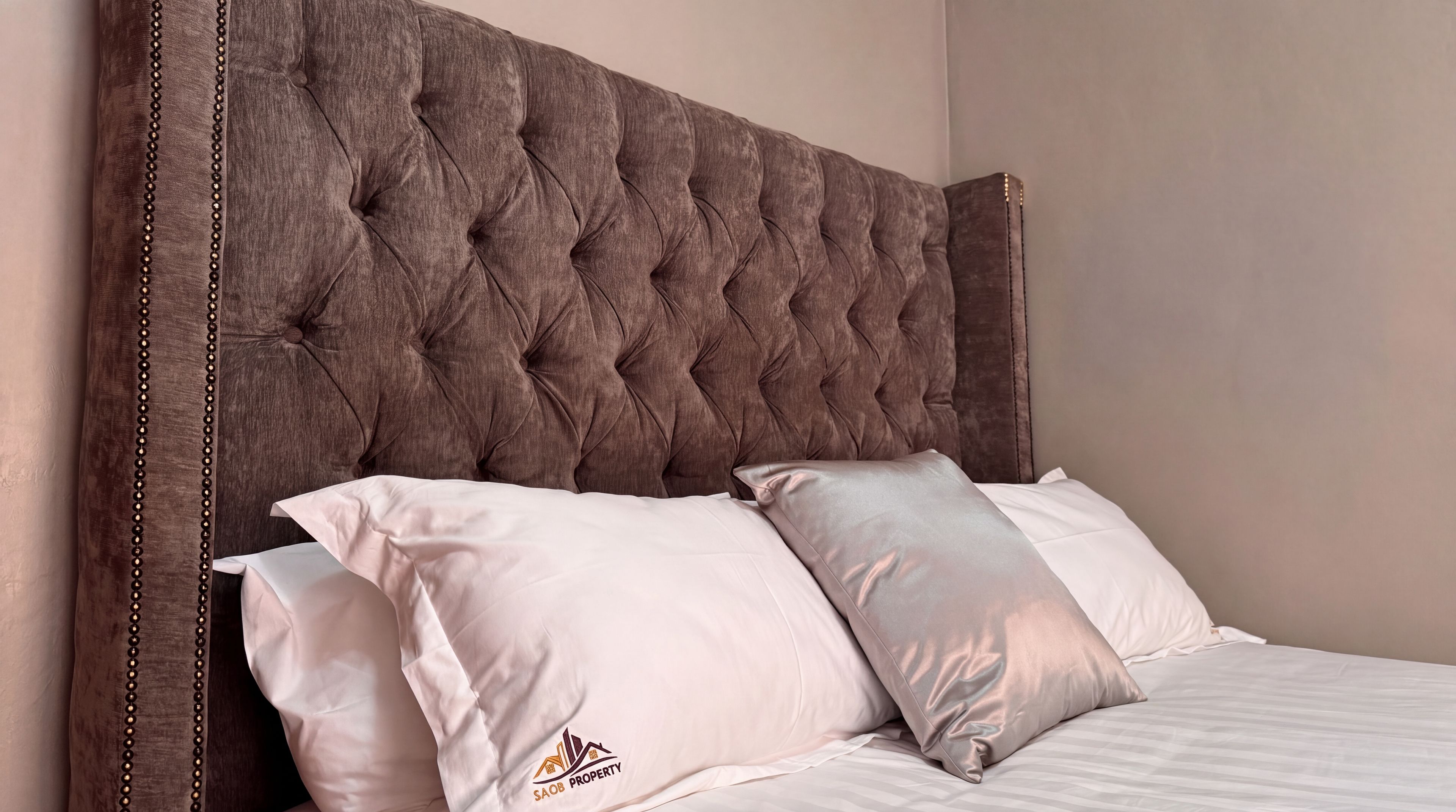 Una cama con cabecera capitonada, dos almohadas y un logotipo en la funda.