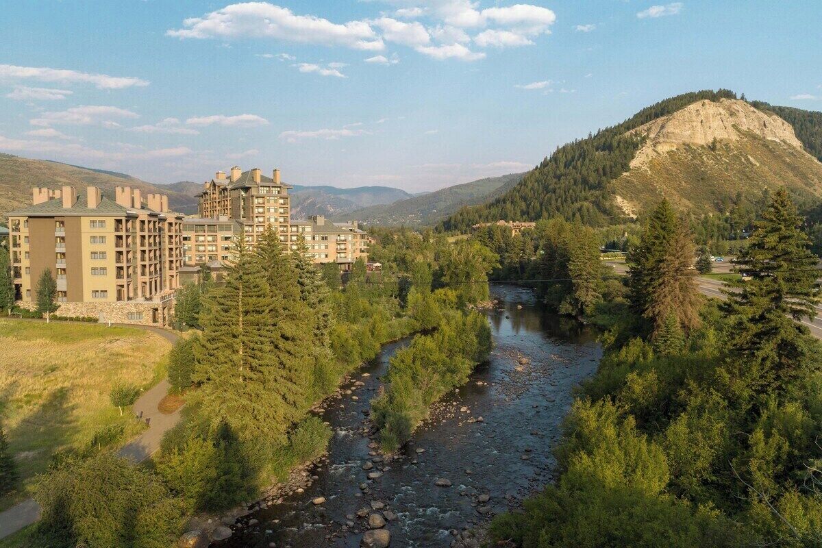 Un hotel de varios pisos, con un río que atraviesa la propiedad y una montaña al fondo.