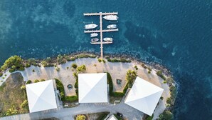 Vista aérea de una propiedad costera con un puerto deportivo, sombrillas blancas y una playa.