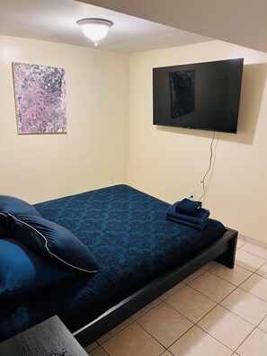 A bedroom with a bed, a television mounted on the wall, and a ceiling light fixture. - Queens NYC Private One Bedroom Basement Apartment (Queens)