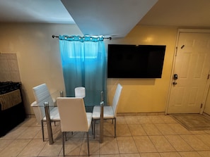 A dining area with a glass table and chairs, a TV mounted on the wall, and a door to the right. - Queens NYC Private One Bedroom Basement Apartment (Queens)
