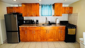 A kitchen with wooden cabinets, a stainless steel refrigerator, a microwave, a coffee maker, and a stove. - Queens NYC Private One Bedroom Basement Apartment (Queens)