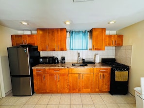 A kitchen with wooden cabinets, a stainless steel refrigerator, a microwave, a coffee maker, and a stove. - Queens NYC Private One Bedroom Basement Apartment (Queens)