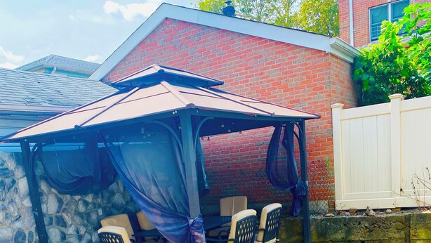 A covered patio area with a stone wall, a white fence, and a grassy lawn. - Queens NYC Private One Bedroom Basement Apartment (Queens)