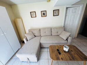 A living room with a sectional sofa, a wooden coffee table, and a remote control on it. - Queens NYC Private One Bedroom Basement Apartment (Queens)