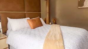 Una cama bien tendida con cabecera, mesita de noche y un reloj de pared.