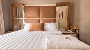 A hotel room with a large bed, a wooden headboard, a bedside table with a clock, and a mirror. - Saob Property South AF (Germiston)