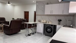 A modern kitchen with a built-in washer and dryer, a dining area with leather chairs, and a marble backsplash. - Saob Property South AF (Germiston)