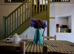 A table with a checkered tablecloth, a vase with purple flowers, a teapot, and a cup. A staircase with green railings is in the background. - Charming Irish Cottage Offering Peace, Comfort and Stunning Lough View (Londonderry)