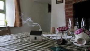 A table with a house-shaped object emitting smoke, a glass jar with a spoon, and a floral teacup on a checkered tablecloth. - Charming Irish Cottage Offering Peace, Comfort and Stunning Lough View (Londonderry)