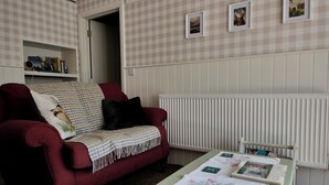 A living room with a red sofa, a table with a quilt, and a radiator. - Charming Irish Cottage Offering Peace, Comfort and Stunning Lough View (Londonderry)