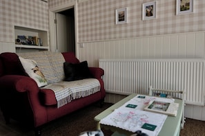 A living room with a red sofa, a table with a quilt, and a radiator.