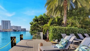 Eine Lounge am Wasser mit Liegestühlen, einem Pool und einer Stadtkulisse im Hintergrund.
