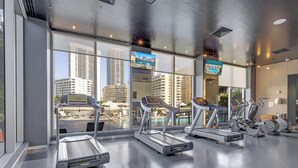 Ein Fitnessstudio mit Laufbändern, Ergometer und Blick auf ein Schwimmbad.