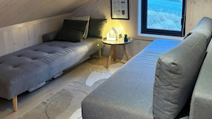 Acogedor dormitorio en ático con cama en altillo, un sofá, una mesita con lámpara y ventana con vistas.