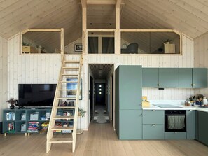 Un espace de vie compact doté d’une mezzanine, d’une cuisine aux armoires de couleur turquoise et d’une échelle en bois menant à l’étage supérieur.