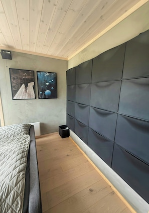 A bedroom with a bed, a headboard, a wall-mounted TV, and a small trash bin.