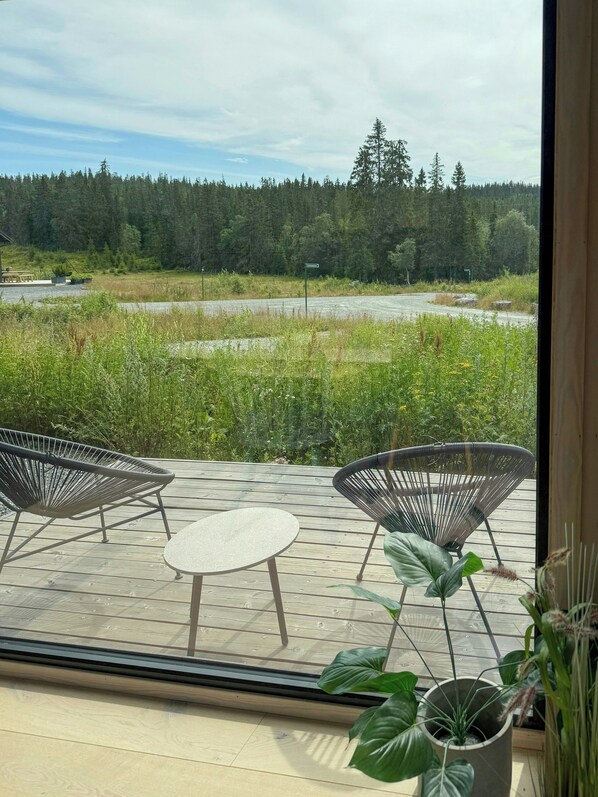 Une terrasse en bois avec deux chaises et une table, donnant sur une zone boisée et un plan d’eau.