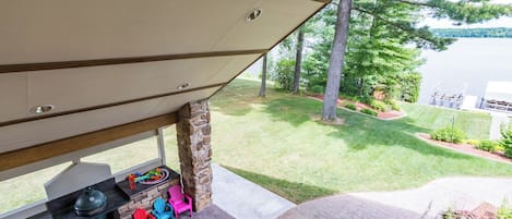 A covered outdoor area with a barbecue grill, colorful Adirondack chairs, and a view of a lake.