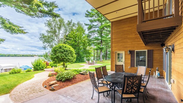 Um alpendre coberto com mesa e cadeiras, vista para um lago e um gramado bem cuidado.