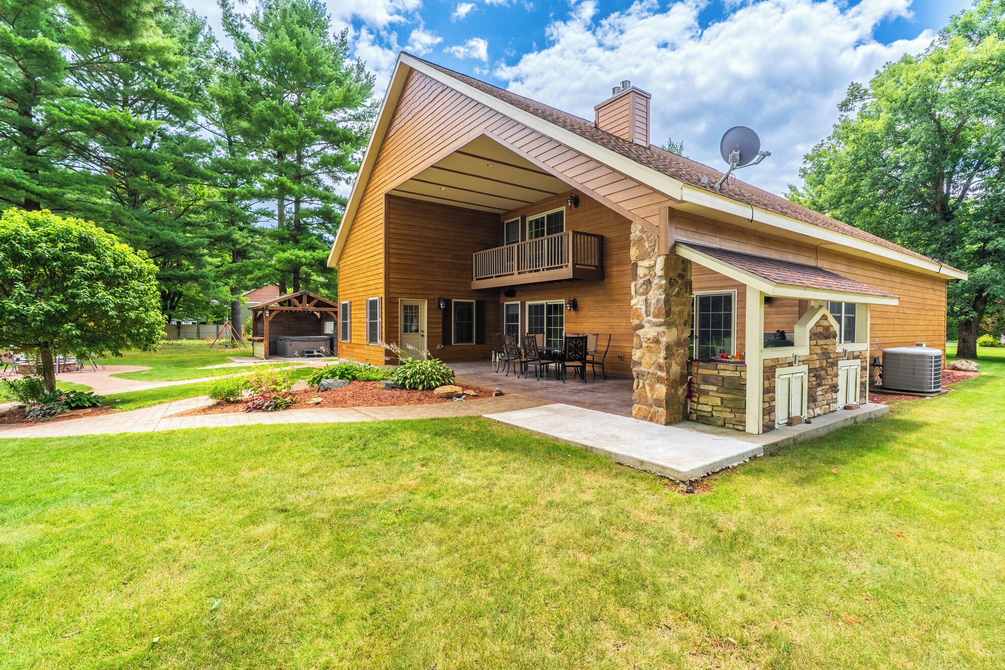 A two-story house with a covered patio, stone foundation, and a satellite dish.