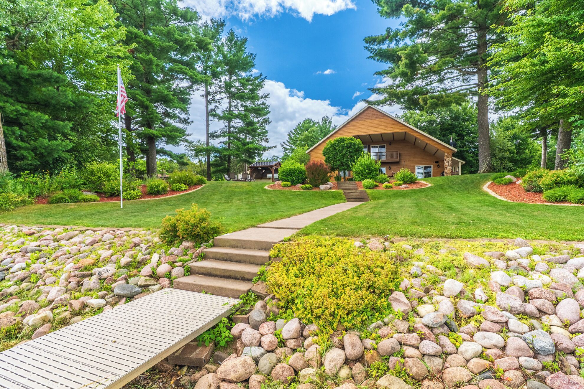 A modern house with a wooden exterior, surrounded by a well-maintained lawn and a variety of trees.