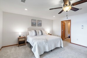 A bedroom with a bed, bedside tables, a ceiling fan, and artwork on the wall.
