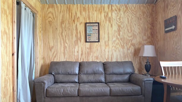 Una habitación con un sofá de cuero marrón, una pared de madera, un cuadro con un gráfico sobre peces, una mesa con una lámpara y una señalización.