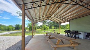 Un espacio al aire libre techado con mesas de picnic y asadores.