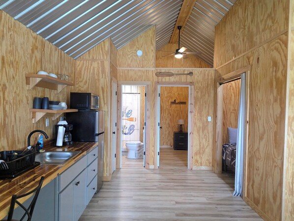 A compact kitchen with wooden walls, a microwave, a sink, and a refrigerator.