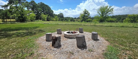 Un pozo de fuego de piedra circular rodeado de postes de madera en un campo cubierto de hierba.