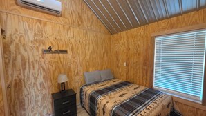 Un dormitorio con cama, mesita de noche, lámpara y aire acondicionado instalado en la pared.