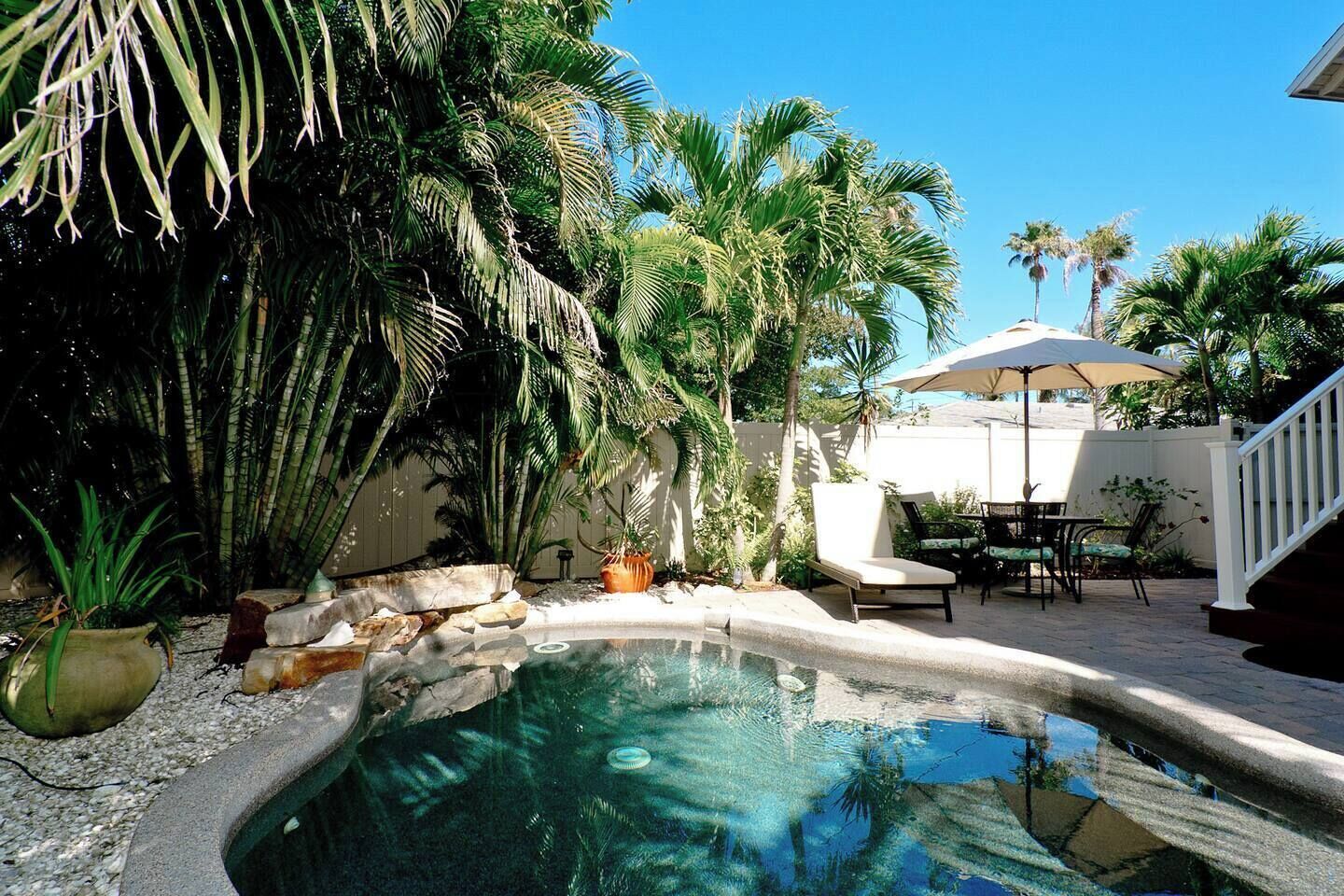 Piscina cercada por plantas tropicais e área de terraço com mobiliário de exterior.